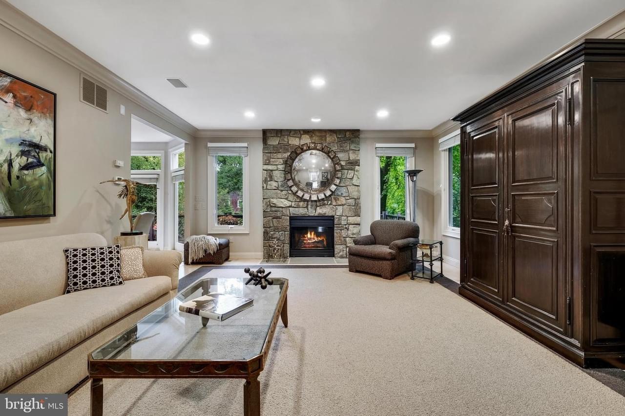 Living roomw ith light colored walls, sofa on the left, large dark wood cabinet on the right, many windows, and a stone fireplace with a round mirror above it